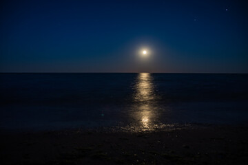 Wall Mural - During the night, a bright full moon illuminates the ocean under the sky