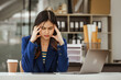 © M+Isolation+Photo - Young woman and other Asian individuals in formal suits work at desks with laptops, addressing concerns such as office syndrome, ergonomics, musculoskeletal disorders, and computer vision syndrome.