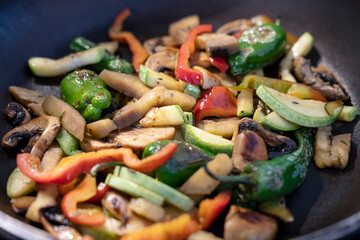 Colorful mix of sauteed vegetables in a pan: sliced mushrooms, zucchini, red, yellow and green bell peppers, lightly cooked veggies used in a healthy stir-fry or as a perfect side dish or main course