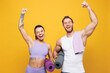 © ViDi Studio - Young fun strong fitness trainer instructor sporty two man woman wear blue clothes spend time in home gym hold yoga mat do winner gesture isolated on plain yellow background Workout sport fit concept