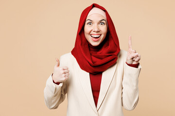 Wall Mural - Young Arabian Asian Muslim woman wear red abaya hijab suit clothes hold index finger up with great new idea show thumb up isolated on plain beige background UAE middle eastern Islam religious concept