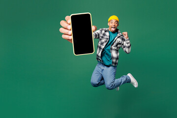Wall Mural - Full body young man of African American ethnicity wear shirt blue t-shirt yellow hat jump high use hold mobile cell phone with blank screen area isolated on plain green background. Lifestyle concept.
