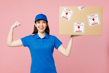 Sticker - Delivery girl employee woman wear blue cap t-shirt uniform workwear work as dealer courier hold cardboard box with fragile text show biceps muscles isolated on plain pink background. Service concept.