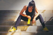 © Panumas - Tired runner woman with a bottle of electrolyte drink freshness after training outdoor workout at the stadium stairway.