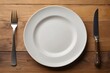 © Adam - Empty white plate with knife and fork isolated on a wooden background. Top view.