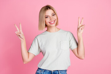 Poster - Portrait of cheerful optimistic girl with bob hairstyle wear white t-shirt showing v-sign symbol isolated on pink color background