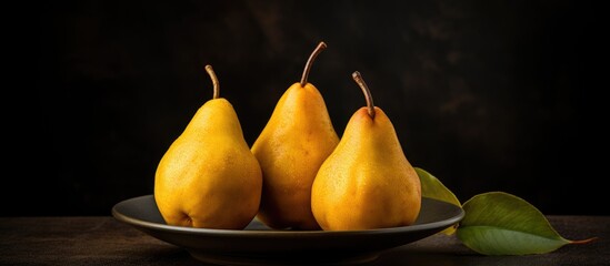 Wall Mural - A copy space image featuring three ripe pears arranged on a plate against a dark background