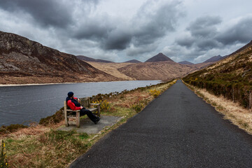 Wall Mural - Man in red jacket sit on wood bench lakeshore Silent Valley Reservoir Moure Mountains Lake Northern Ireland UK Europe