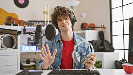 Smiling man with headphones in a music studio surrounded by instruments and recording equipment.