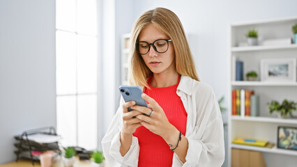 Sticker - A focused young woman using her smartphone in a modern office setting.