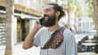 © Krakenimages.com - A cheerful young hispanic man with a beard talking on a phone while walking on a city street.