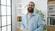 © Krakenimages.com - Handsome hispanic man with beard smiling in an office, exuding professionalism and approachability.