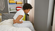 © Krakenimages.com - African american woman feeling abdominal pain in a comfortable bedroom setting, portraying health and lifestyle themes.