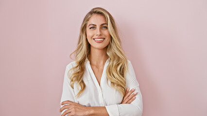 Wall Mural - Cheerful young blonde woman standing confidently with arms crossed, expressing joy and happiness over a pink isolated background!