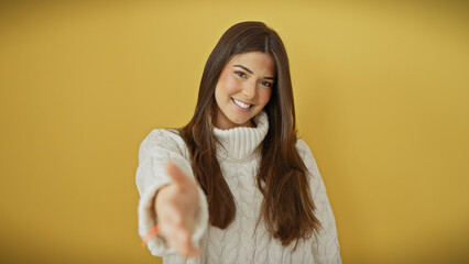 Canvas Print - A cheerful young hispanic woman in a white sweater offering a handshake against a yellow background.