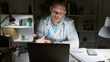 Sticker - A hispanic male doctor in a white coat gestures during a video call in a dimly lit clinic office at night