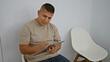 © Krakenimages.com - Serious latin guy, relaxed yet concentrated, sits in chair taking notes. indoor portrait of young hispanic man writing job interview checklist on clipboard in waiting room background.