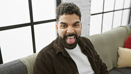 Sticker - A cheerful young man with a beard sits in a modern living room, providing a candid indoor portrait.