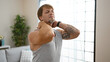 © Krakenimages.com - Man stretching neck muscles at home, showing tattoos in a casual, light-filled living room setting.