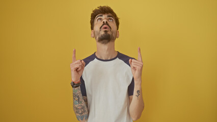 Poster - Hispanic man with beard pointing upwards isolated over yellow background.