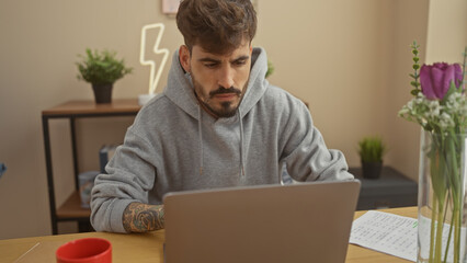 Canvas Print - A focused hispanic man with a beard works on a laptop at a home office, showcasing productivity and a casual lifestyle.