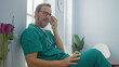 © Krakenimages.com - Hispanic male doctor in green scrubs listening to a voice message in a bright hospital room