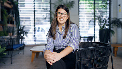 Canvas Print - Young beautiful hispanic woman smiling confident sitting on a chair at the office