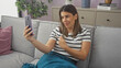 © Krakenimages.com - Smiling woman taking selfie on couch in modern apartment