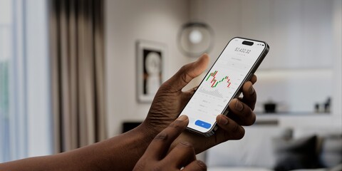A user interacts with a stock trading app on a smartphone, displaying market charts and data, in a modern home setting. Fictional app 