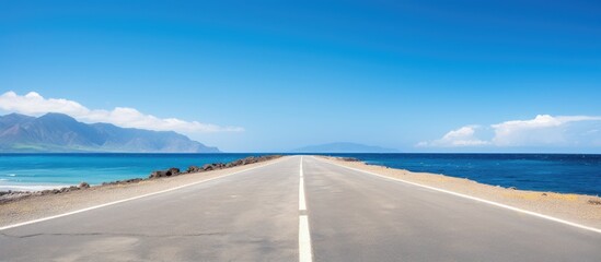 Aufkleber - An empty asphalt road with copy space image borders a serene beach under a clear blue sky.