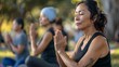 © iuricazac - A serene scene of a woman in a black tank top with a tattoo on her arm sitting in a yoga pose with her eyes closed surrounded by other individuals in a park
