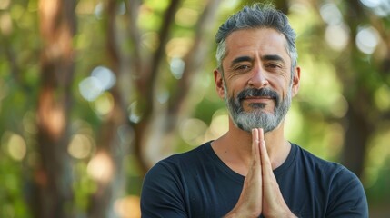 Sticker - Man with gray beard and hair wearing black shirt standing in front of blurred trees hands clasped together in prayer or meditation pose.
