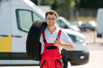 Young smiling man, in red coverall,  car mechanic holding auto tires