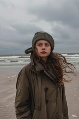 Poster - A woman standing alone on a sandy beach with the vast ocean stretching out behind her, ideal for use in scenes depicting solitude, contemplation or relaxation