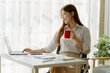 © Kritdanai - Adorable businesswoman holding coffee cup while working in the office room.