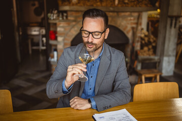 Adult man sit in a winery and hold glass of wine and clipboard