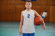 © Zamrznuti tonovi - A junior basketball player is standing indoor at court with ball.