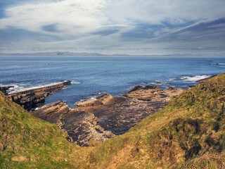 Wall Mural - The ocean is calm and the sky is blue. The water is clear and the rocks are brown. Rough stone coast of Ireland. Mullaghmore area. Loved by tourist shore with stunning Irish nature scenery.