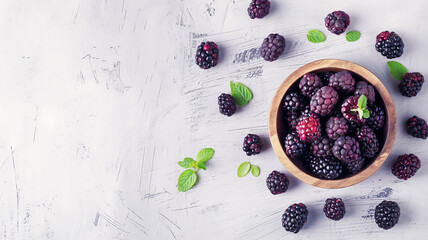 Wall Mural - A wooden bowl filled with blackberries, garnished with mint leaves, with some berries and mint scattered on a textured white background.
