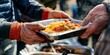 © RealPeopleStudio - A close-up of a volunteer handing a hot meal to a homeless person at a soup kitchen