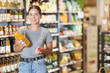 © JackF - In bio ecological goods store, girl buyer carefully examines and view product, bottle of juice. Young female customer gets acquainted with unconventional and unfamiliar drink