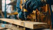 © Nature Creative - Closeup male carpenter hand in gloves using electric drill to assemble the wood in the carpentry shop