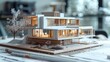 © admin_design - A detailed architectural model of a modern house with large windows and a tree in the foreground. The model is set on a wooden base and surrounded by architectural drawings.