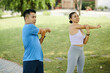 © DragonImages - Man and woman in athletic wear stretching their arms together during an outdoor workout in the park