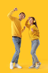 Wall Mural - Young couple in headphones dancing on yellow background
