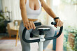 © DragonImages - A detailed view of hands gripping the handlebars of an exercise bike, with the display panel in focus