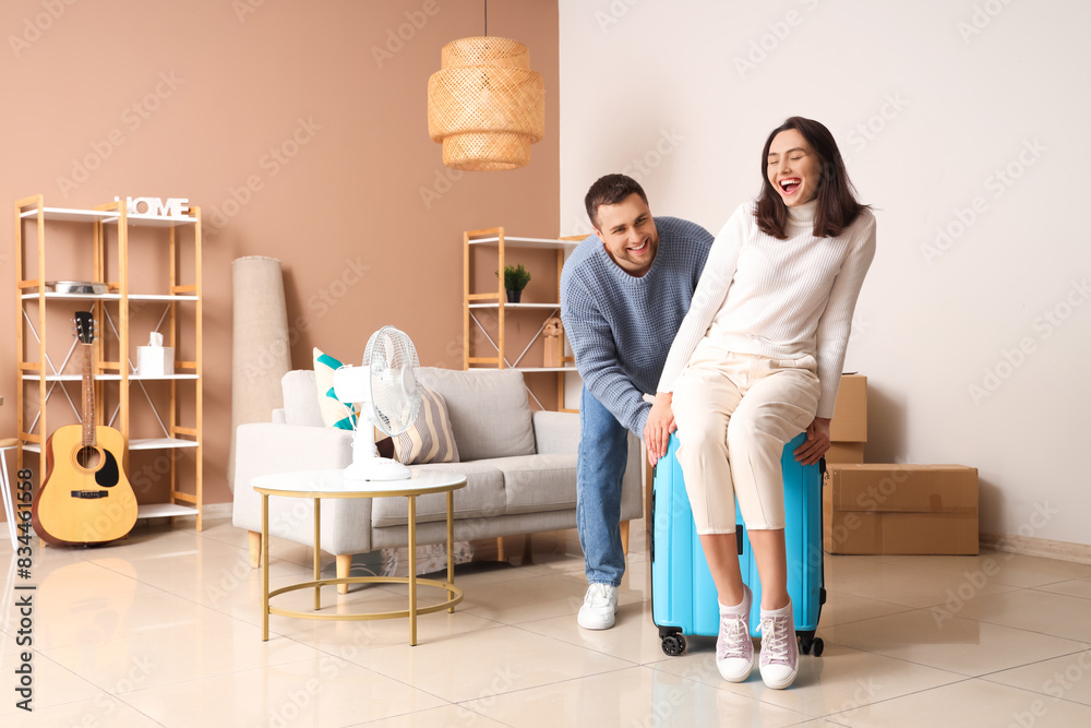 Happy young couple with suitcase in room on moving day