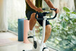 © DragonImages - A man in workout clothes riding a stationary bike indoors, with plants visible through a large window