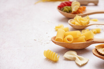 Wall Mural - Wooden spoons with different uncooked pasta on light background, closeup