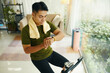 © DragonImages - A man in workout attire checking his fitness tracker while exercising on a stationary bike indoors